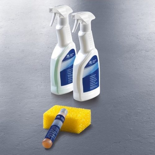 Drei Sommerpflegeprodukte (Sprayflaschen, Schwamm) auf grauem Untergrund arrangiert.