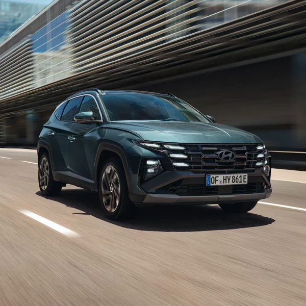 Hyundai TUCSON fährt auf einer mehrspurigen Straße vor einem modernen Bürogebäude, aufgenommen in Bewegung.